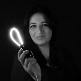 Nunzia Acquaviva portrait holding black heart-shaped light fixture, white glow, dark hair, direct gaze, black background, focused lighting.
