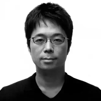 Black and white portrait of Tokujin Yoshioka, a man with short dark hair, wearing rectangular glasses and a v-neck shirt.