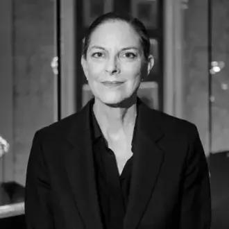 Black and white portrait of Johanna Grawunder wearing a tailored black blazer, showing facial lines and a blurred interior background.