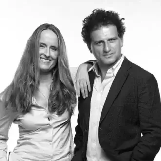 Black and white portrait of a woman in a light shirt and a man in a dark blazer, studio shot with neutral lighting.