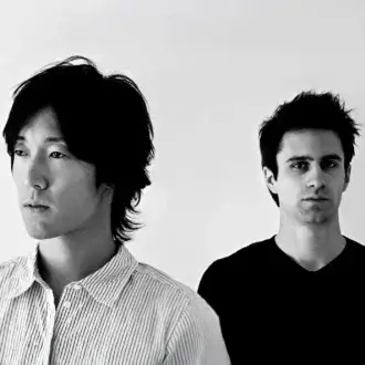 Two men portrait, fair skin, dark hair, striped shirt and black V-neck, white background, minimalist composition, even lighting, facial details.