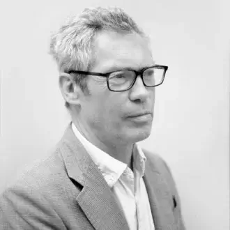 Jasper Morrison portrait, gray hair, dark glasses, tweed blazer, profile view, neutral expression, light gray background, soft lighting.
