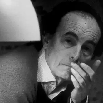 Black and white portrait of Giuseppe Ostuni in a suit, hand to mouth, with diffused light from a rounded lampshade and textured wall backdrop.