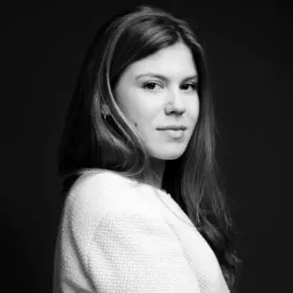 Black and white portrait of a woman with wavy dark hair wearing a cream knit sweater, featuring Federica Farina, against a dark background.