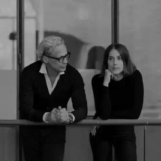 Black and white portrait of a man and woman in a modern interior with glass panels, minimalist architecture, and soft, natural lighting.
