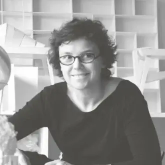 Constance Guisset portrait, black and white, short curly hair, glasses, architectural shelving backdrop, soft diffused lighting.