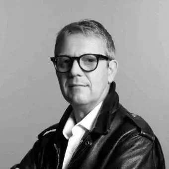 John Bennett portrait, black leather jacket, white shirt, gray hair, rectangular glasses, neutral gray background, soft lighting.
