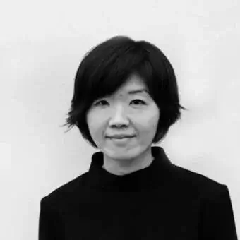Black and white portrait of a woman with short dark hair, wearing a black turtleneck against a white backdrop, neutral expression.