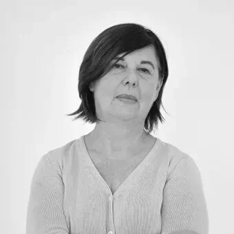 Black and white portrait of a woman with short dark hair, wearing a light knit sweater, arms crossed, neutral expression, plain background.