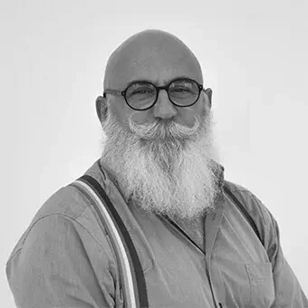 Bald man Luigi Glorini, white beard and mustache, dark glasses, light shirt with striped suspenders, neutral expression, gray background.