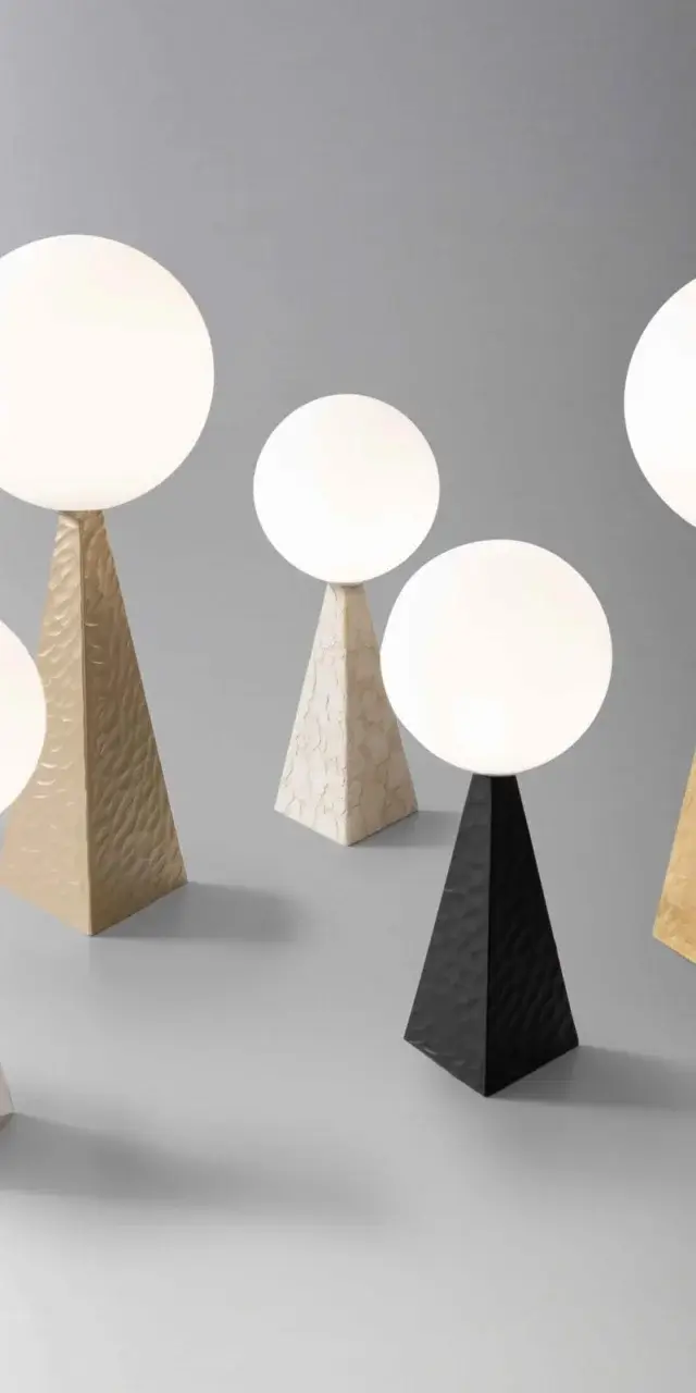 Stillux lamps with opaque white globes on textured gold, silver, black, and marble pyramid bases, studio lighting.