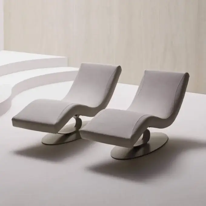 Lounge chairs, beige fabric upholstery, curved backrests on dark metal circular bases, positioned against vertically paneled light gray walls.