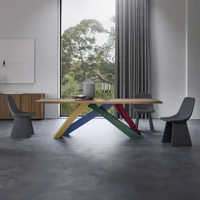 Dining table with geometric base, light wood top, gray chairs, and sideboard in a modern room with concrete floor and artwork.