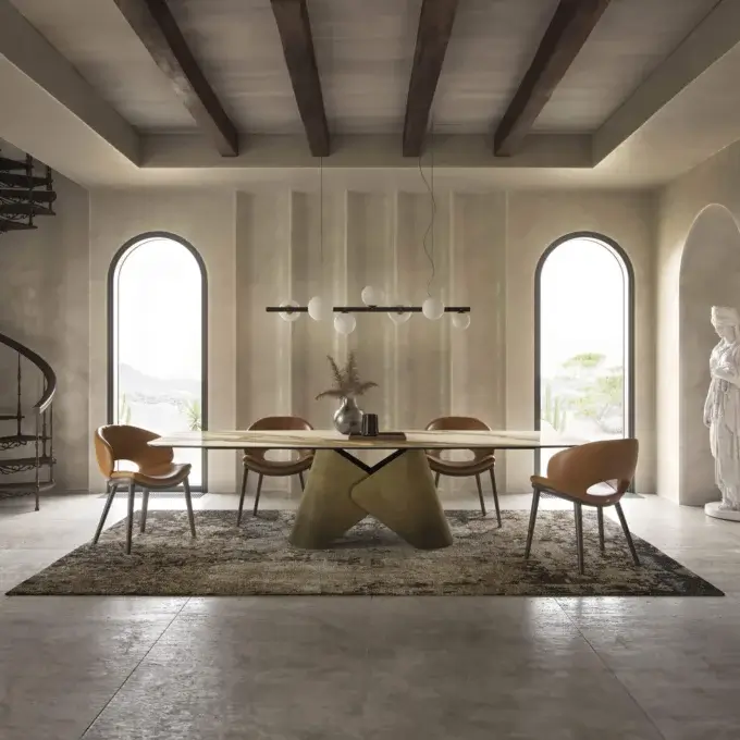 Dining table with light wood top and dark bronze base, surrounded by six tan leather chairs, under a linear pendant light.