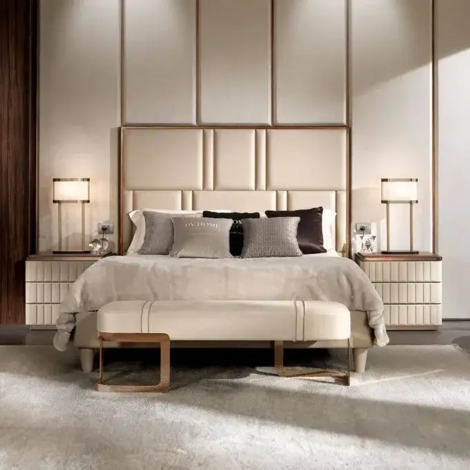 King bed with padded headboard, warm wood frame, cream duvet, brass lamps, and grey rug in neutral bedroom setting.