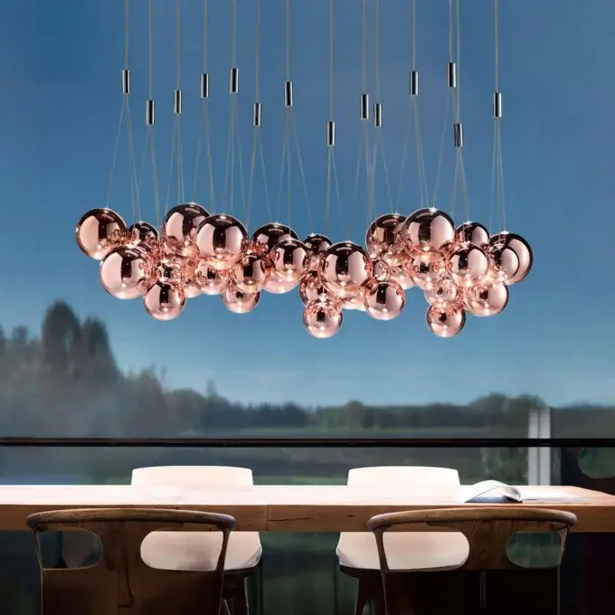 Lodes chandelier with rose gold orbs hangs over dark wood dining table and chairs in modern interior with landscape view.