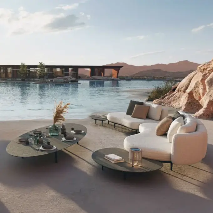 Outdoor sofa set with beige upholstery, oval coffee tables, and desert pool backdrop, featuring modern architecture.