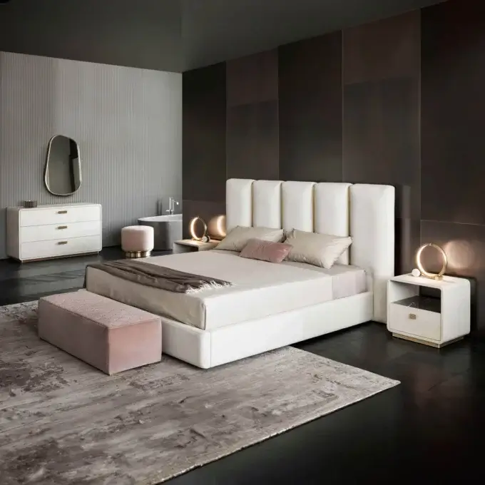 Cassoni Rugiano rug, rectangular, distressed gray and beige, under king bed with white upholstered headboard, gold lamps, and blush pink bench.