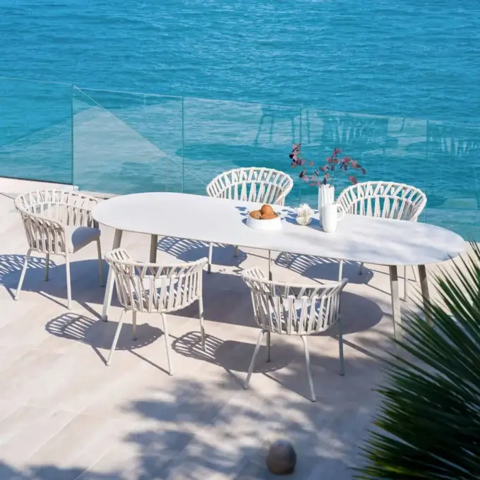 Varaschin dining set with white tabletop and silver metal base, six woven white chairs, ocean view, tiled terrace.