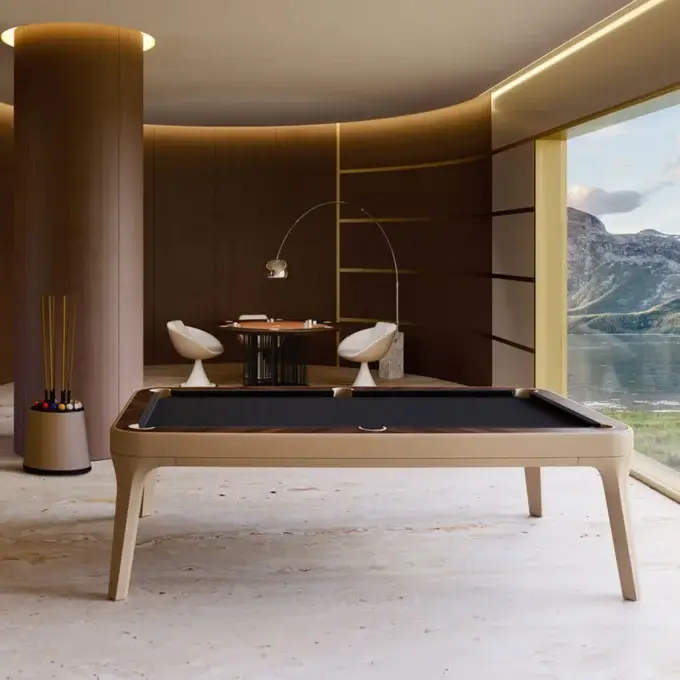 Vismara billiards table, green felt, beige wood frame, with cue rack and round table in a room with wood paneling and mountain view.