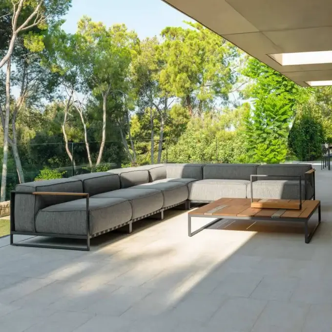 Modular sectional sofa, dark gray fabric, square tufting, with matching wood and metal coffee table on gray tiled patio, shaded by beige awning.