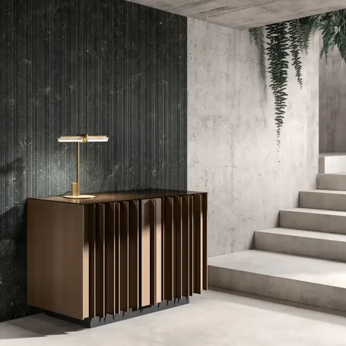 Cassoni Venicem console table, dark brown wood slats, gray base, with brass lamp, against ribbed wall and concrete steps.