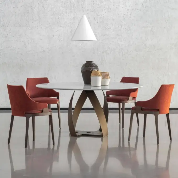 Round dining table with white marble top and brushed brass base, surrounded by four burnt orange fabric chairs, with pendant light.