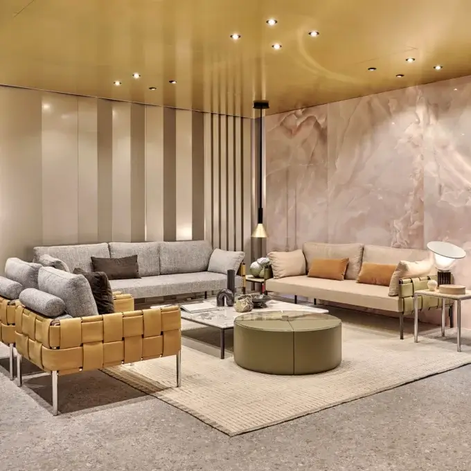 Living room with gray & beige sofas, leather armchair, olive & glass tables, marble wall paneling, gold ceiling, terrazzo floor.