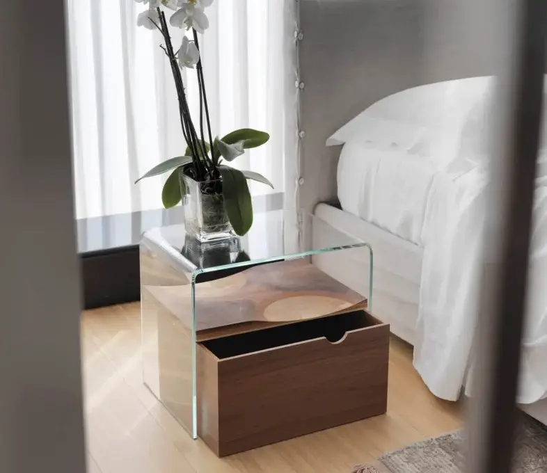 Cassoni Horm Bifronte bedside table, dark wood base, rectangular shape with glass top displaying white orchids in a vase, modern bedroom setting.