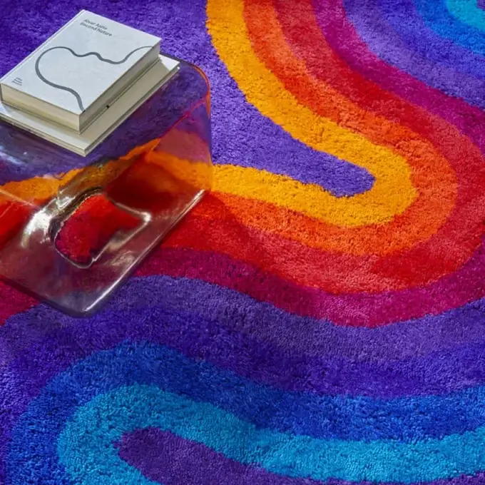 Circular rug, wool blend, psychedelic swirl pattern in blue, purple, orange, and yellow, with acrylic side table and books.