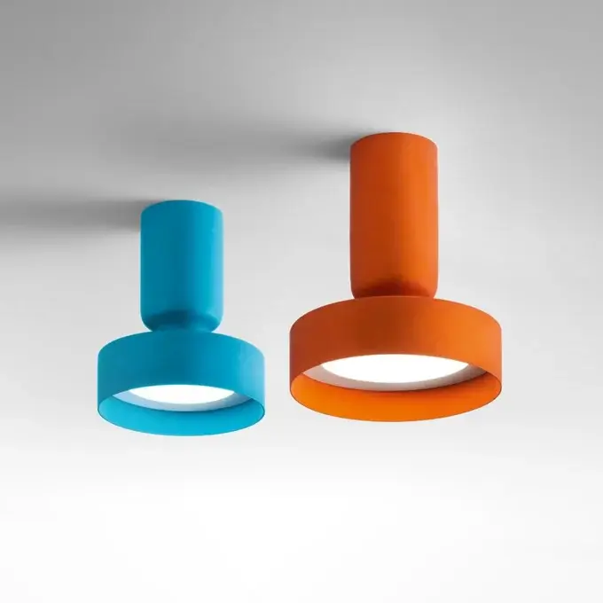 Two cylindrical lamps in turquoise and orange cast bright circular light on a pale gradient background