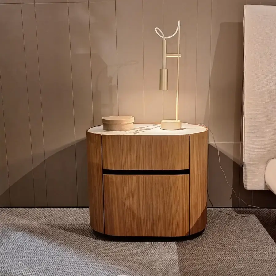Birch nightstand with rounded form and two drawers, featuring a white arched lamp and stone object on a gray rug.