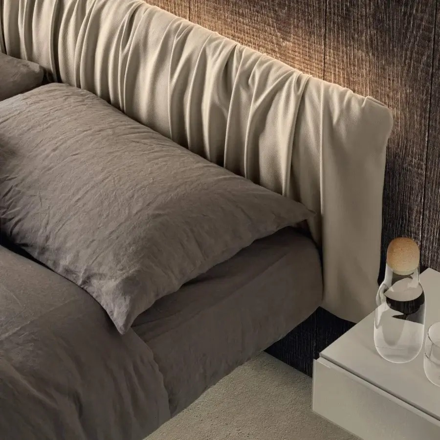 Distinguished Lago Fluttua bed with a light beige textile headboard and rippled texture, appearing to float with muted grey-brown linens