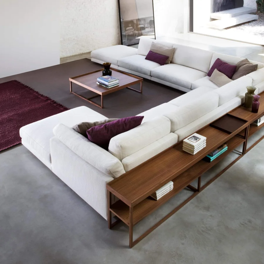 Lavish Swan Italia Host sectional with matte white fabric upholstery, purple and brown accent pillows, and brown wooden shelves