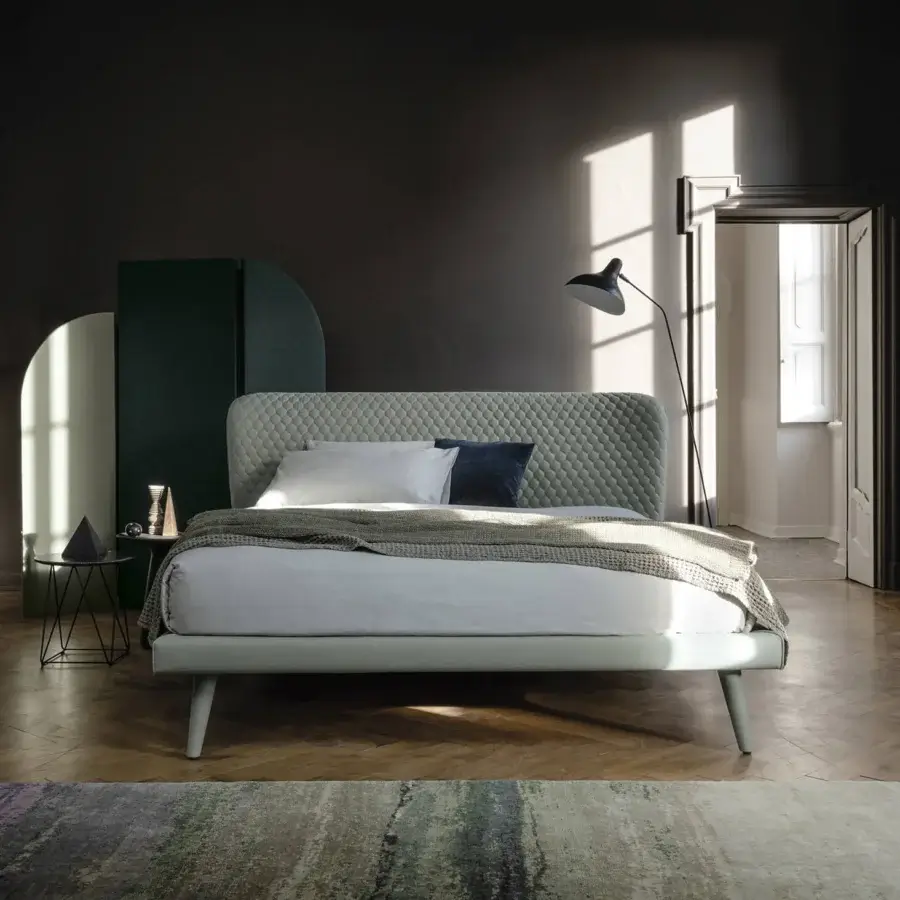 Refined Bolzan Letti Corolle bed with padded capitonné headboard and tapered light gray wood legs upholstered in light gray textile