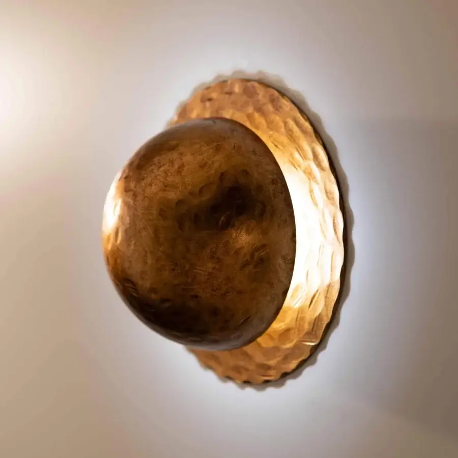 Distinguished Stillux Orbis wall lamp with a hammered metal surface in golden-brown, emitting ambient light from a spherical cover