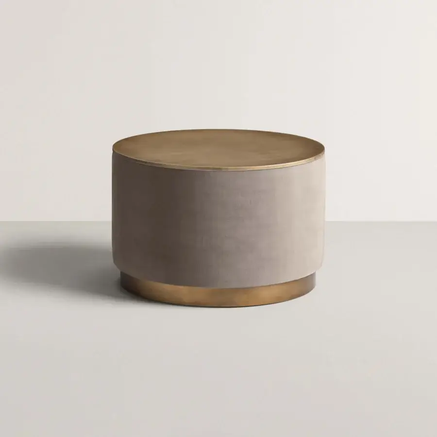 Cylindrical coffee table, taupe velvet upholstery, brushed brass top and base, minimalist design, textural contrast, modern style.