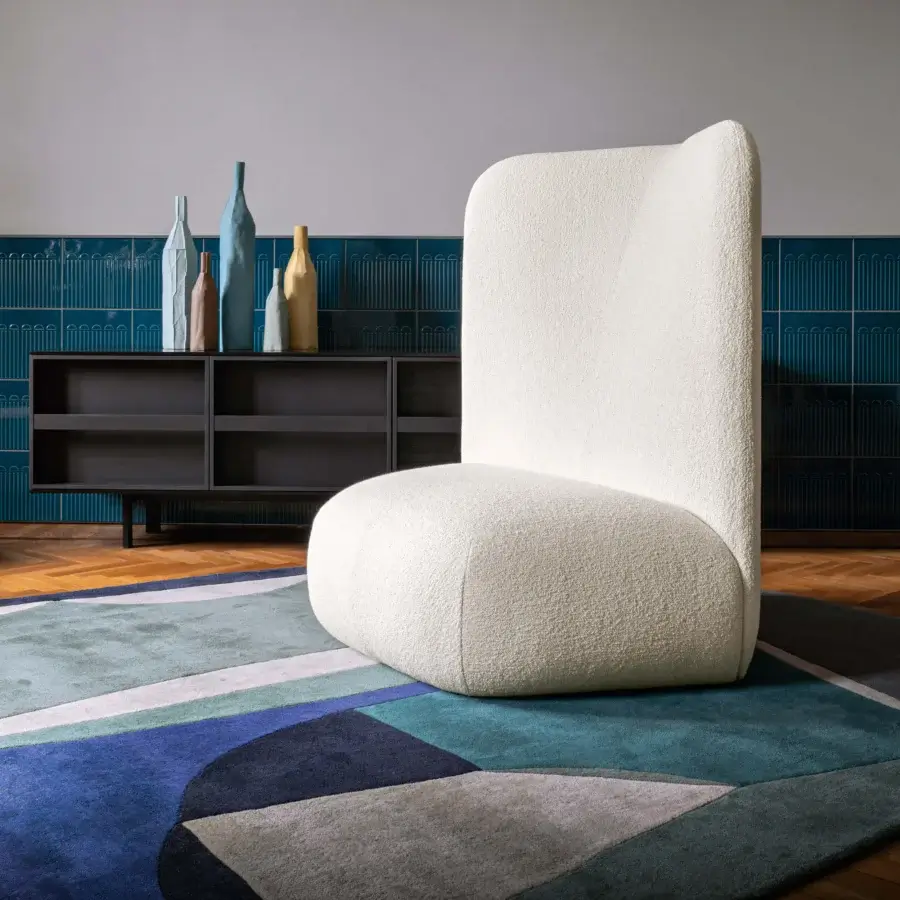 Miniforms Botera lounge chair, off-white fabric, rounded high-back, on geometric blue rug with parquet floor and textured blue wallpaper.