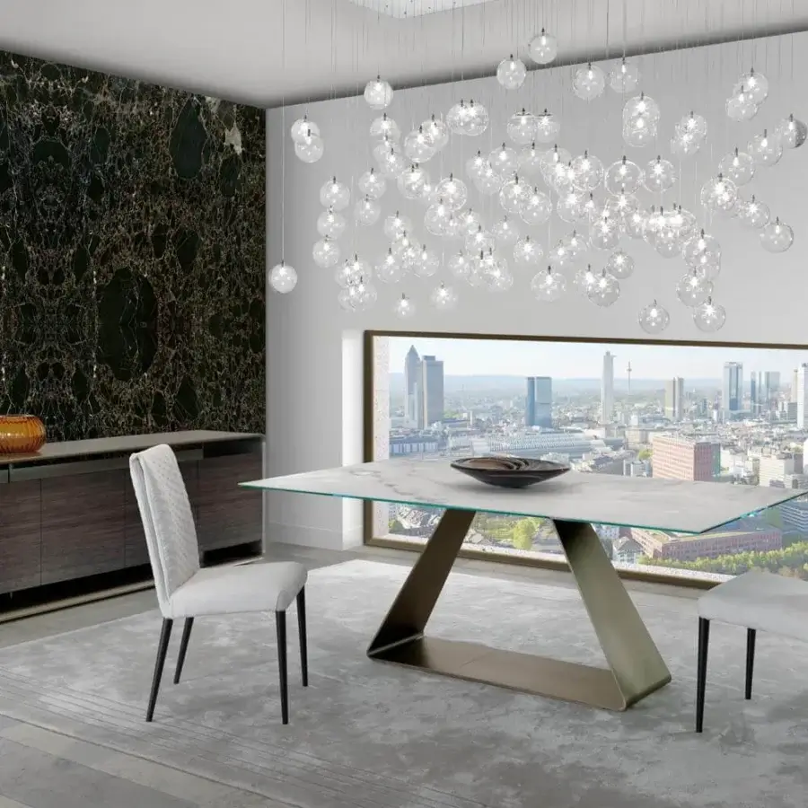Refined Reflex Oh table with a bent metal base in satin bronze and a Marble glass top displaying light gray and white tones