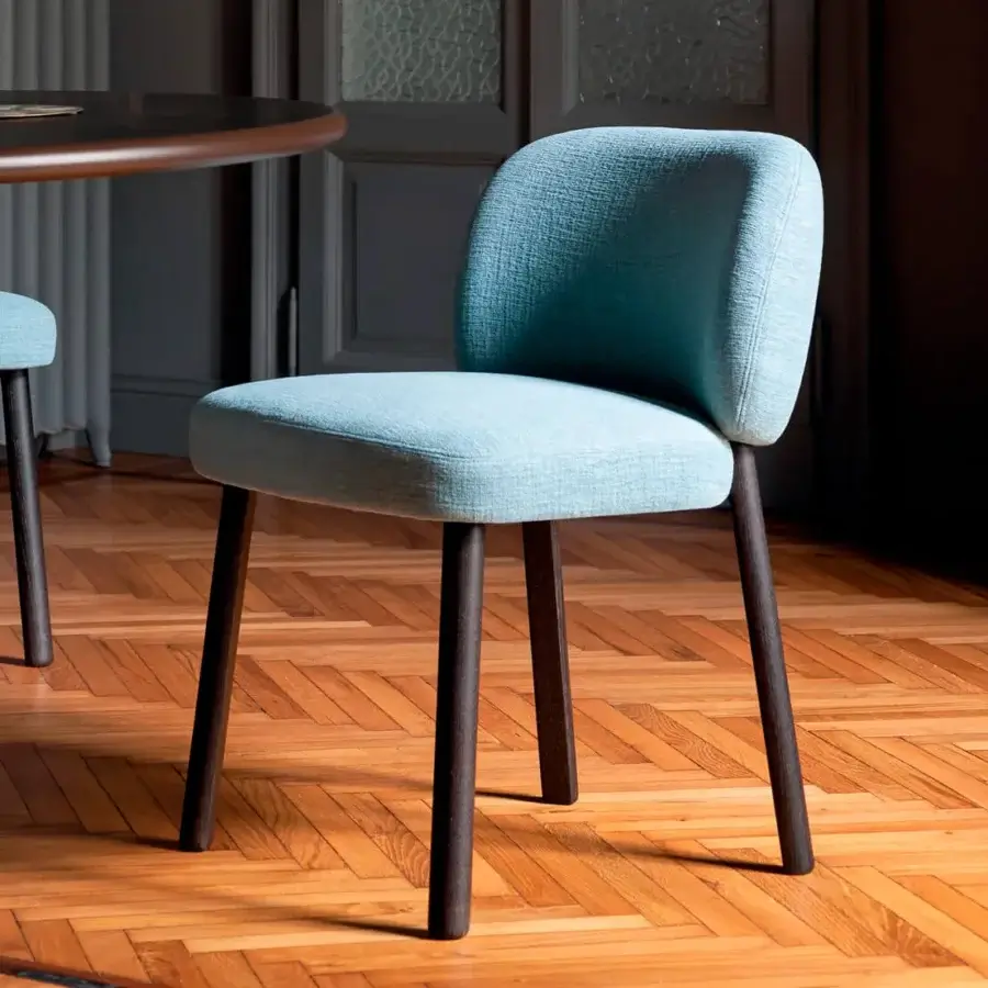 Bross Aretha chair, light blue upholstered fabric, curved back with tapered dark wood cylindrical legs on parquet flooring.