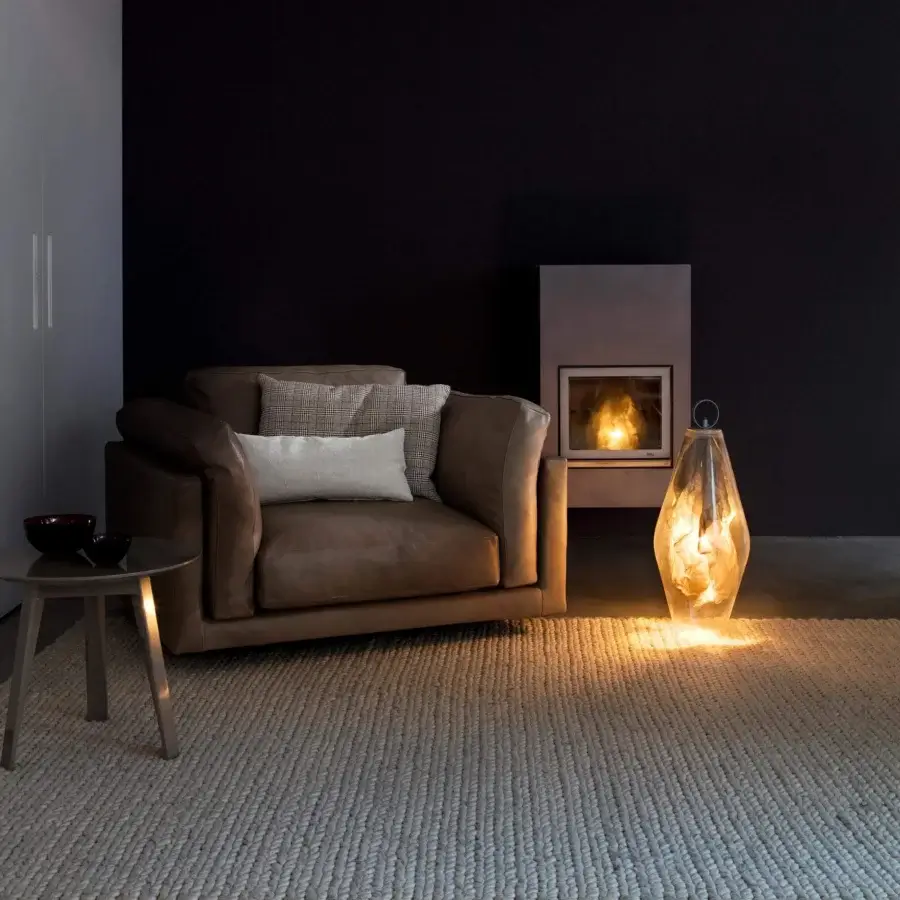 Light brown upholstered seating with patterned cushions beside a gray vertical panel and dark table with a bowl shaped object