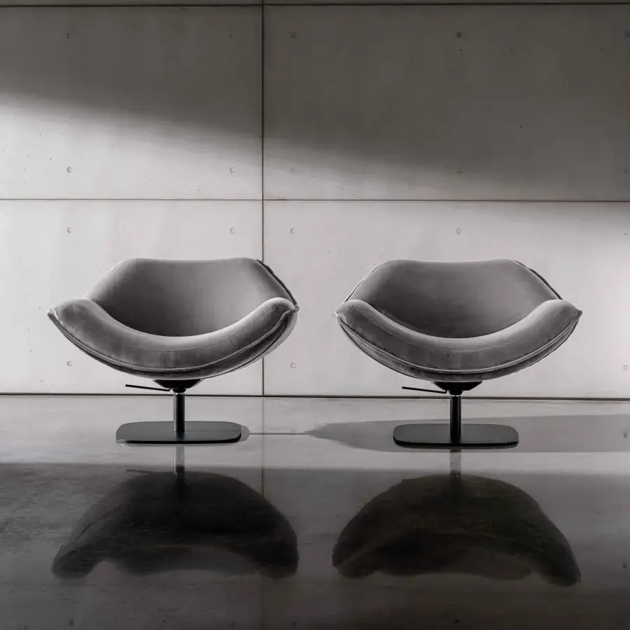 Alisia swivel lounge chairs by Sovet Italia, gray fabric upholstery, rounded biomorphic shape, black circular base, concrete block wall.