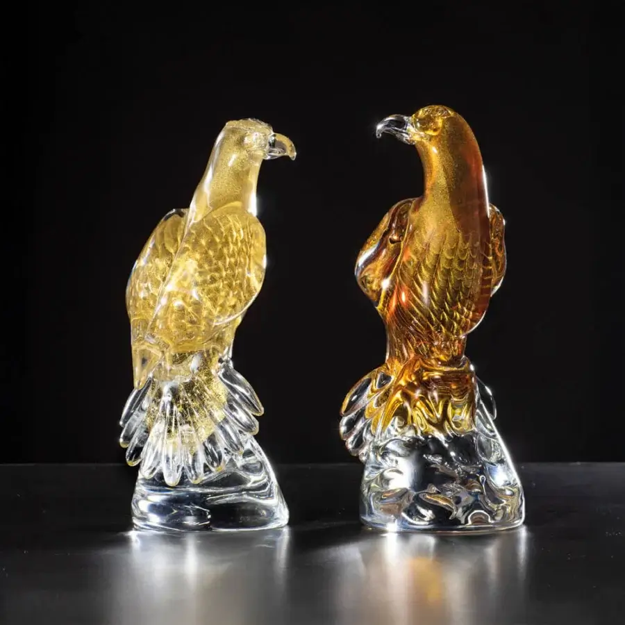 Glass falcon sculptures by Duccio Di Segna with gold & amber flecks displayed on a reflective gray surface, dynamic poses.