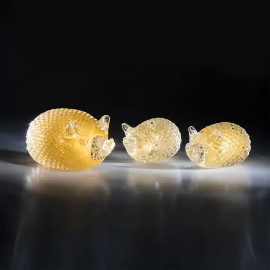 Glass hedgehog sculptures, golden tone, curled pose, arranged in descending size on reflective dark gray surface against black backdrop.