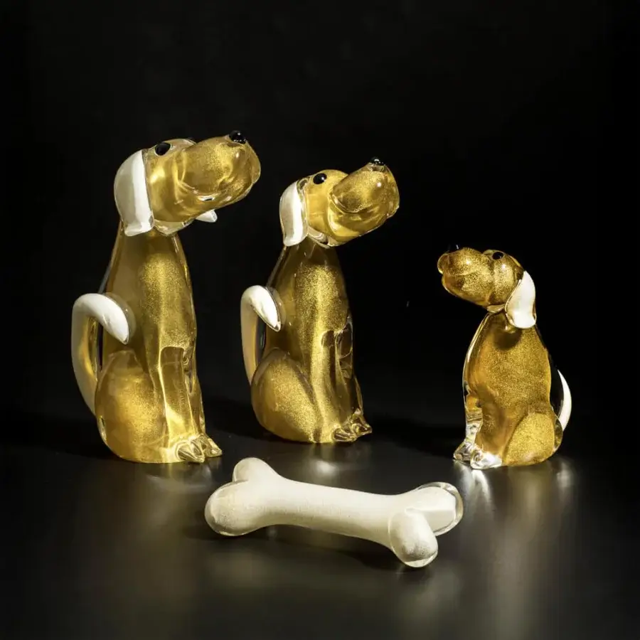 Glass dog sculptures, golden-amber tone, speckled texture, with white accents, arranged with a bone on a black reflective surface.