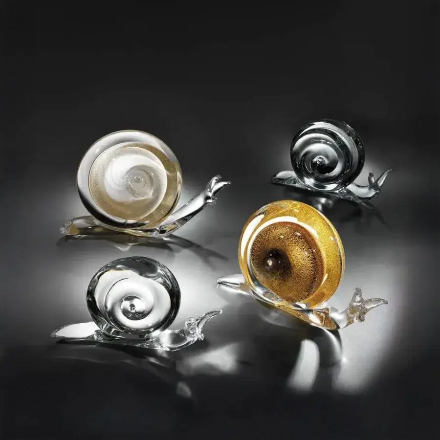 Glass snail sculptures by Duccio Di Segna—gold, amber, gray, champagne shells—spiral forms on black reflective surface.