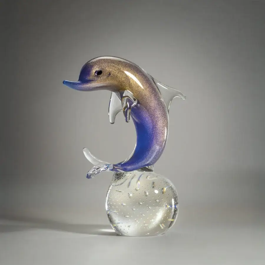 Glass dolphin sculpture with blue, purple, and gold gradient, leaping over a clear sphere on a gray background.