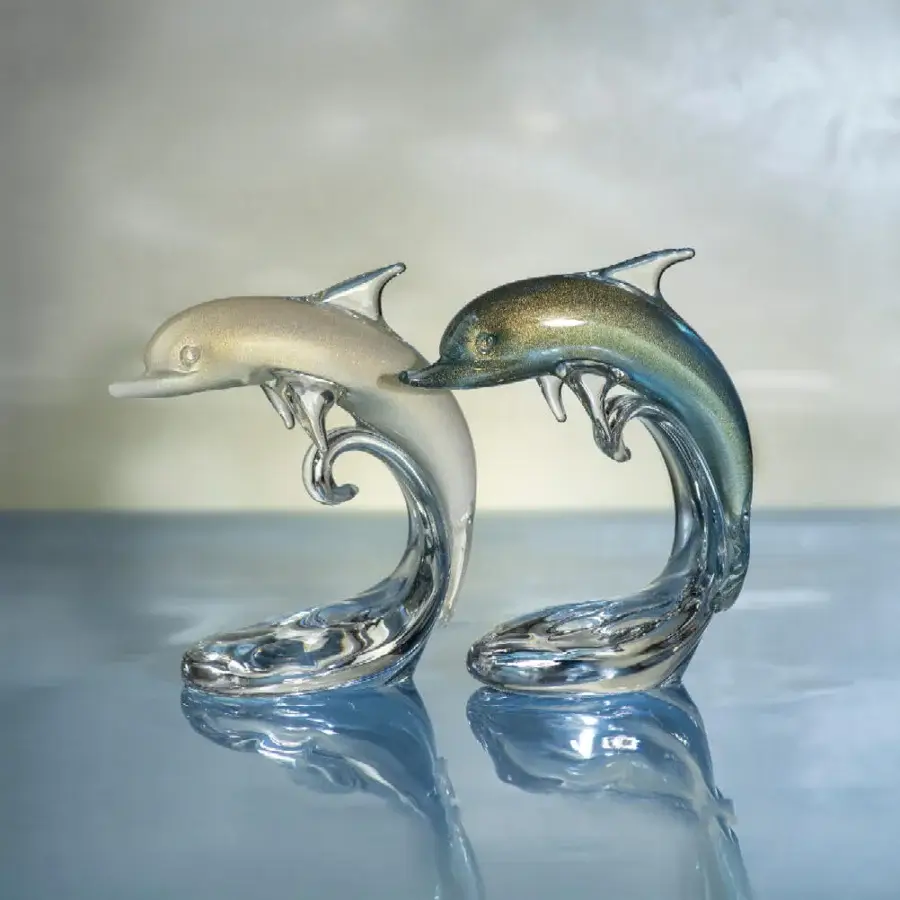 Glass dolphin sculptures, “dolphin baby on the wave” by Duccio Di Segna, feature opalescent cream-to-white and teal-to-green gradients on a blue reflective base.