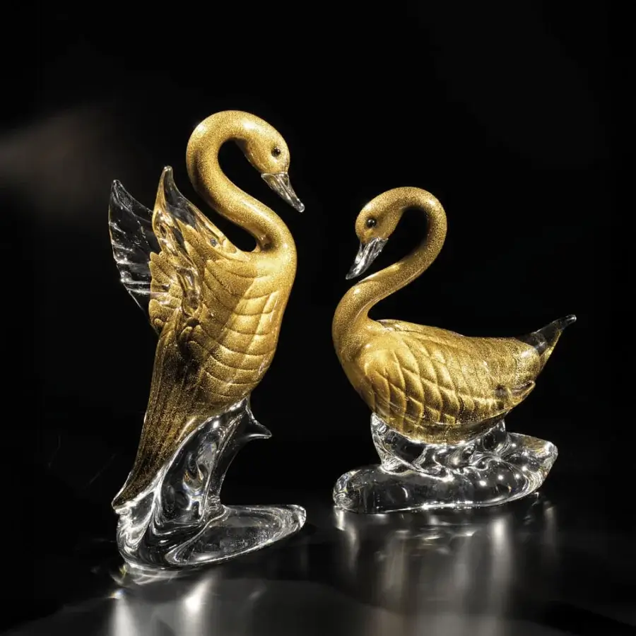 Glass swan sculptures by Duccio Di Segna, gold-toned textured bodies, clear bases, spotlight illumination, fractured wing detail.