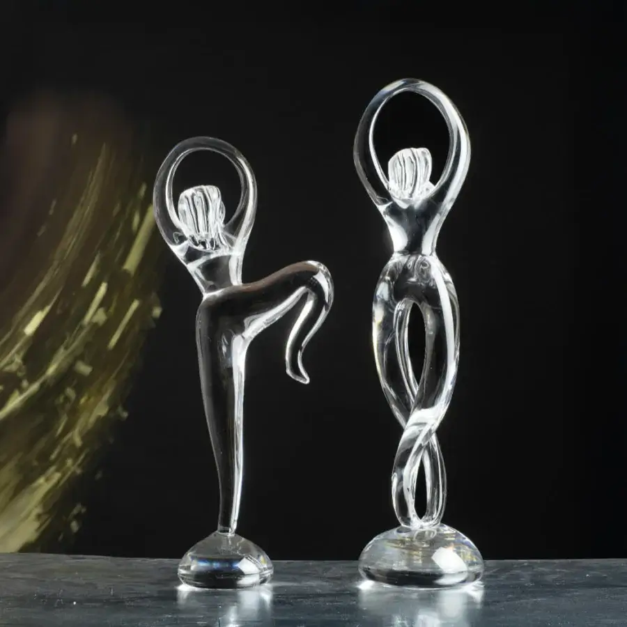 Glass sculptures, transparent human figures by Duccio Di Segna, dynamic poses with elongated forms on dark gray surface against black backdrop.